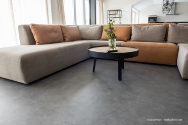 L-förmiges Sofa mit hellbraunen Kissen, einem runden Couchtisch und Blumen in einem modernen Wohnzimmer.