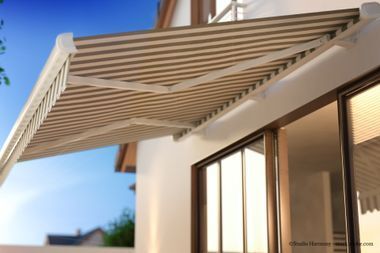 An einem sonnigen Tag ist eine beige-weiß gestreifte, einziehbare Markise über einer Terrassentür ausgefahren.