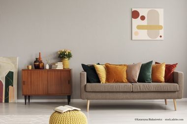 Wohnzimmer mit braunem Sofa, Holzschrank, bunten Kissen und abstrakter Kunst.