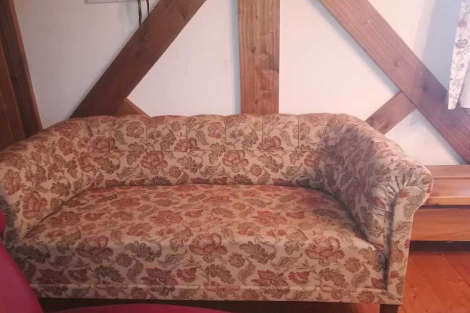 Braunes Sofa mit Blumenmuster vor einer weißen Wand mit Holzbalken.