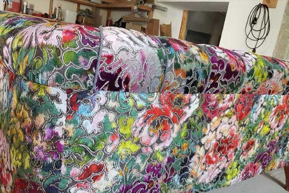 Gepolstertes Sofa mit farbenfrohem floralem Samtmuster in einer Werkstattumgebung.