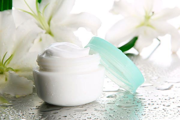 Un tarro de crema está sobre una mesa al lado de flores blancas.