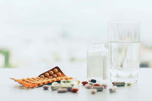 Una mesa llena de pastillas, un vaso de agua y una botella de leche.