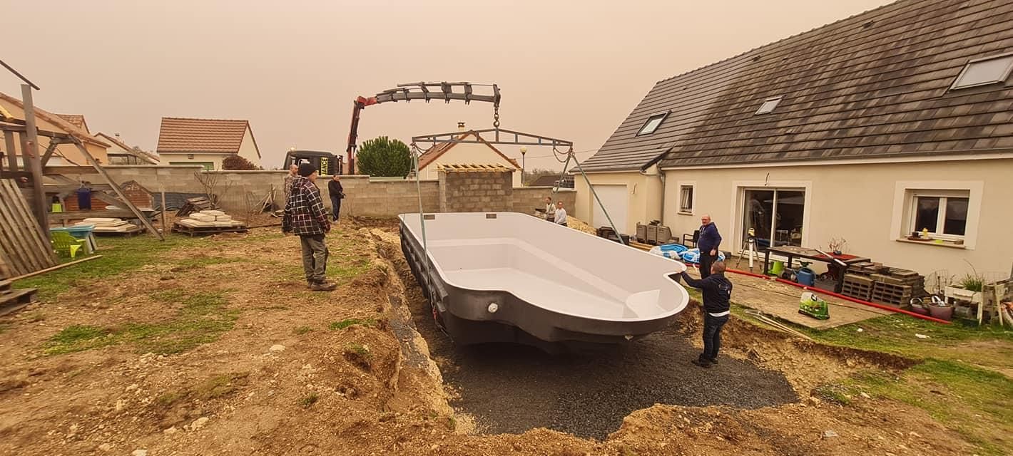 Deux personnes déplacent un petit bateau blanc sur une remorque dans une rue boueuse d’un village.