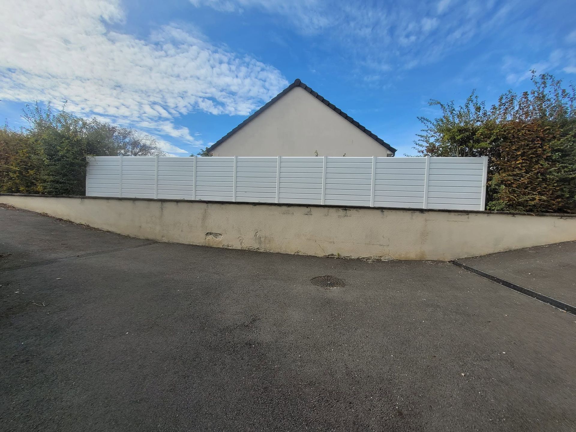 Clôture blanche devant une maison, sur une allée en pente, sous un ciel bleu