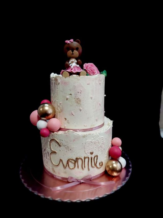 Un pastel de dos niveles con globos y un osito de peluche encima.
