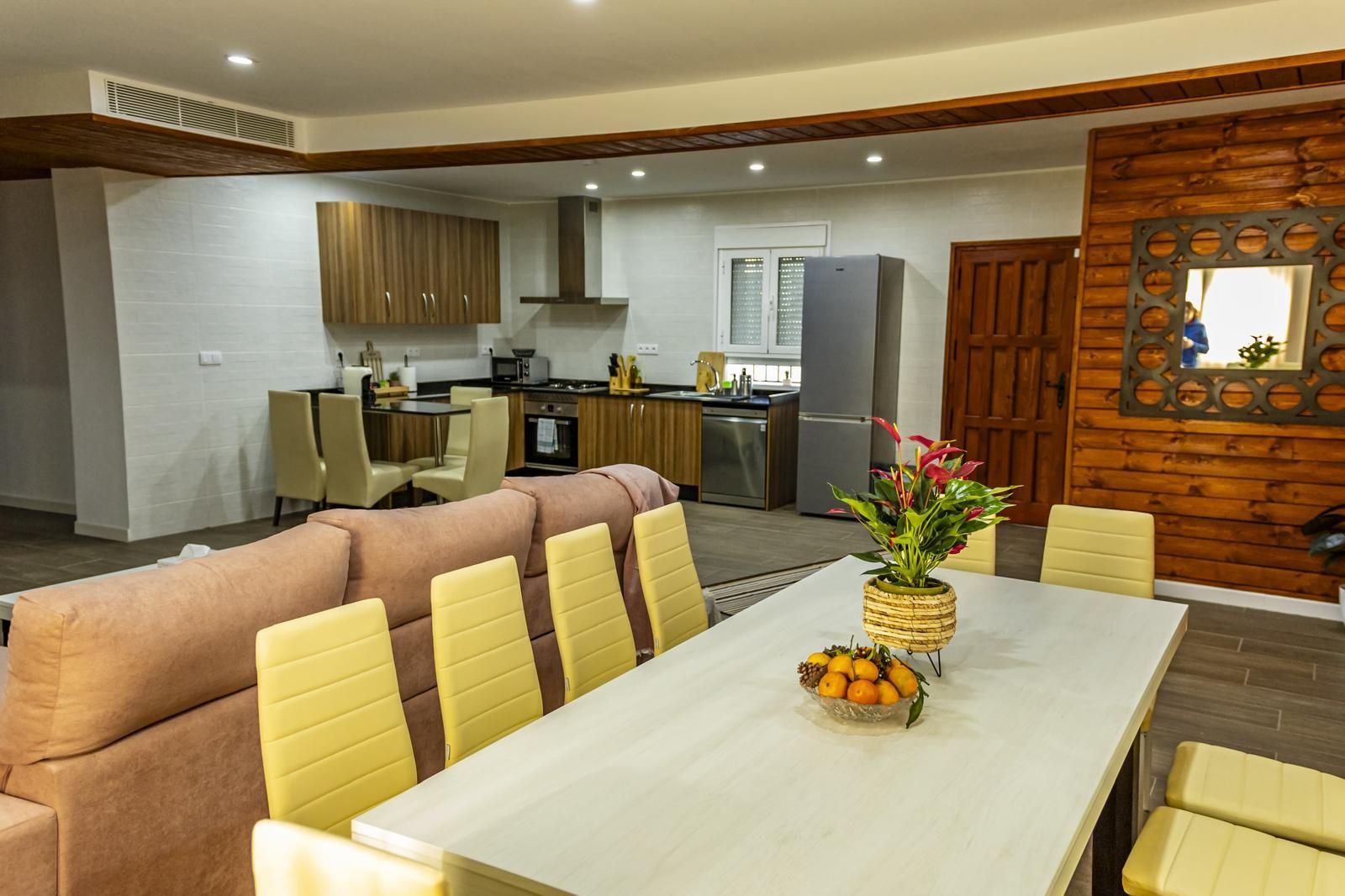 Cocina y comedor de concepto abierto con mesa larga, sillas, sofá y detalles de madera.