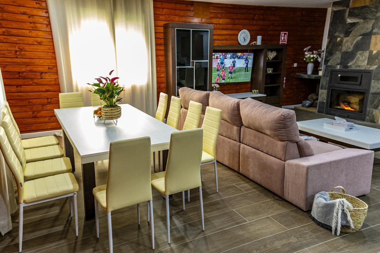 Comedor con una gran mesa blanca, sillas de color amarillo claro y un sofá rosa cerca de una chimenea.