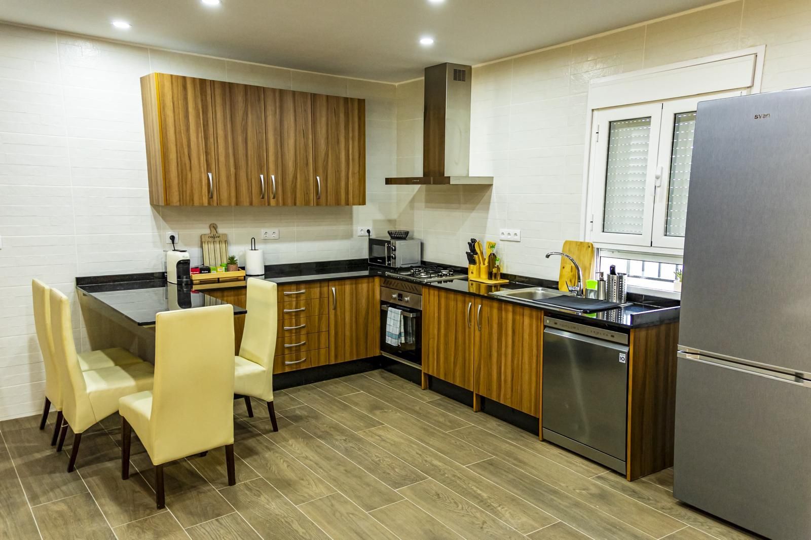 Cocina moderna con gabinetes de madera, electrodomésticos de acero inoxidable y una mesa de comedor con cuatro sillas.