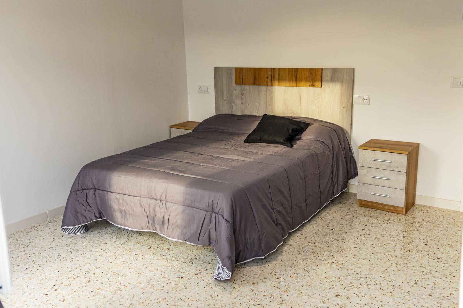 Dormitorio con cama, mesitas de noche y cabecero bicolor sobre suelo de terrazo.