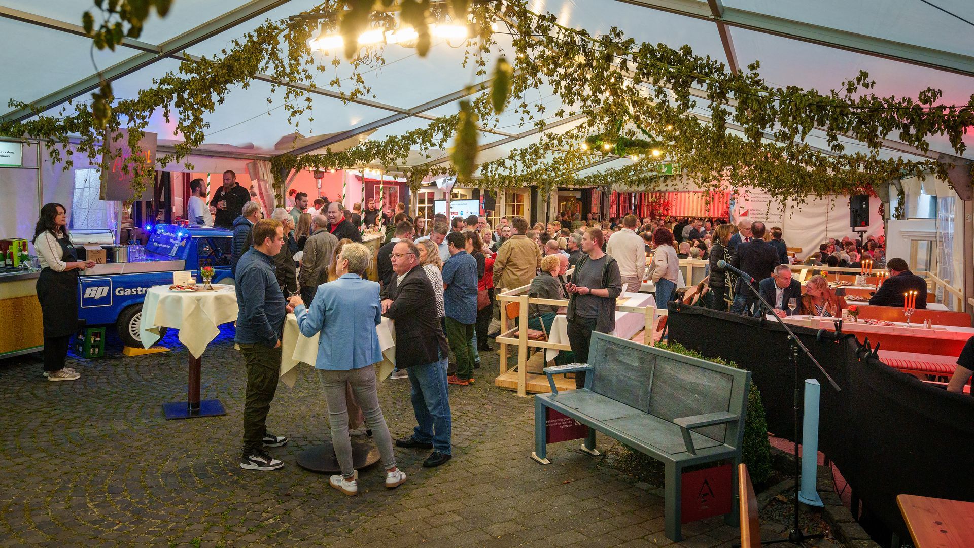 Markthalle mit hängenden Pflanzen, Menschen, die an Ständen stöbern, und einem grauen Sofa im Vordergrund