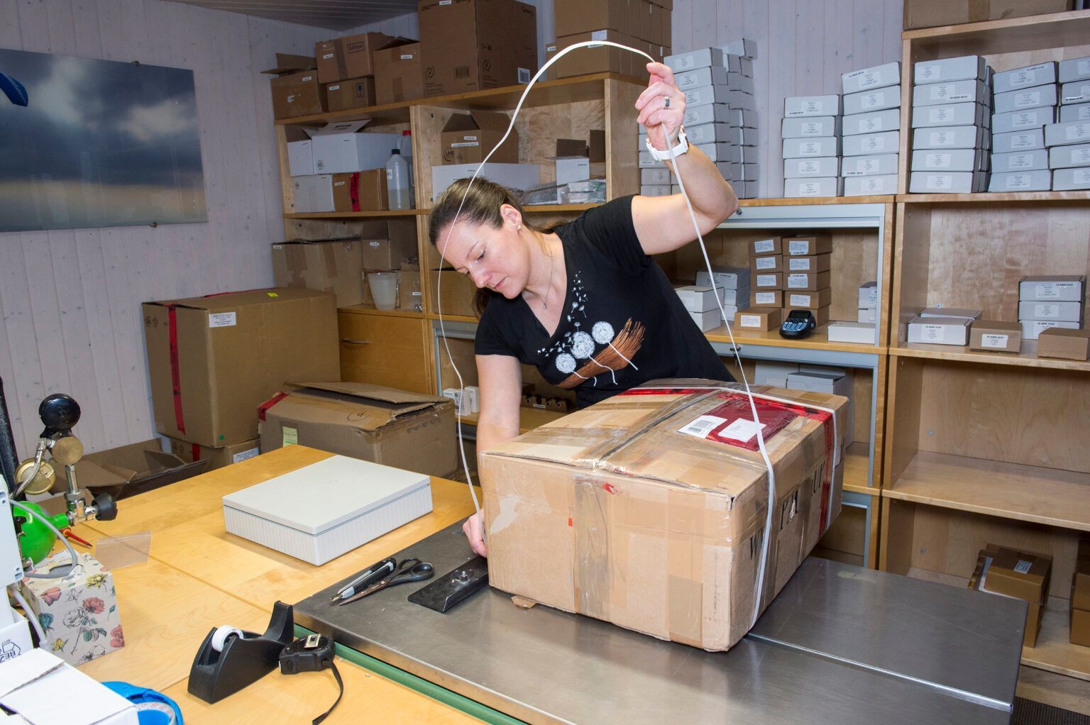 Frau im schwarzen Hemd verpackt in einem kleinen Lagerhaus einen Karton mit Schnur.