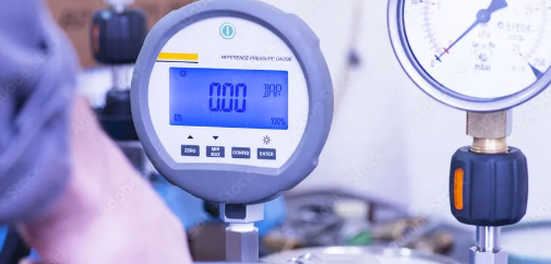 Eine Hand hält ein weißes digitales Thermometer mit der Anzeige 33,2 in einem Schaltschrank mit Kabeln und einem kleinen Ventilator.