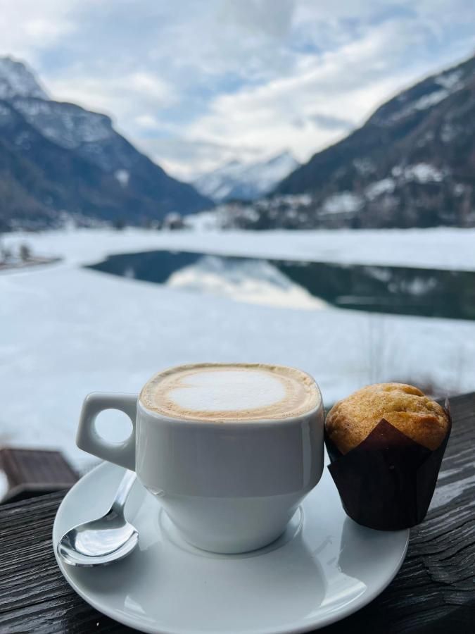 Tazza di cappuccino e muffin su un piattino, con montagne innevate e un lago sullo sfondo.