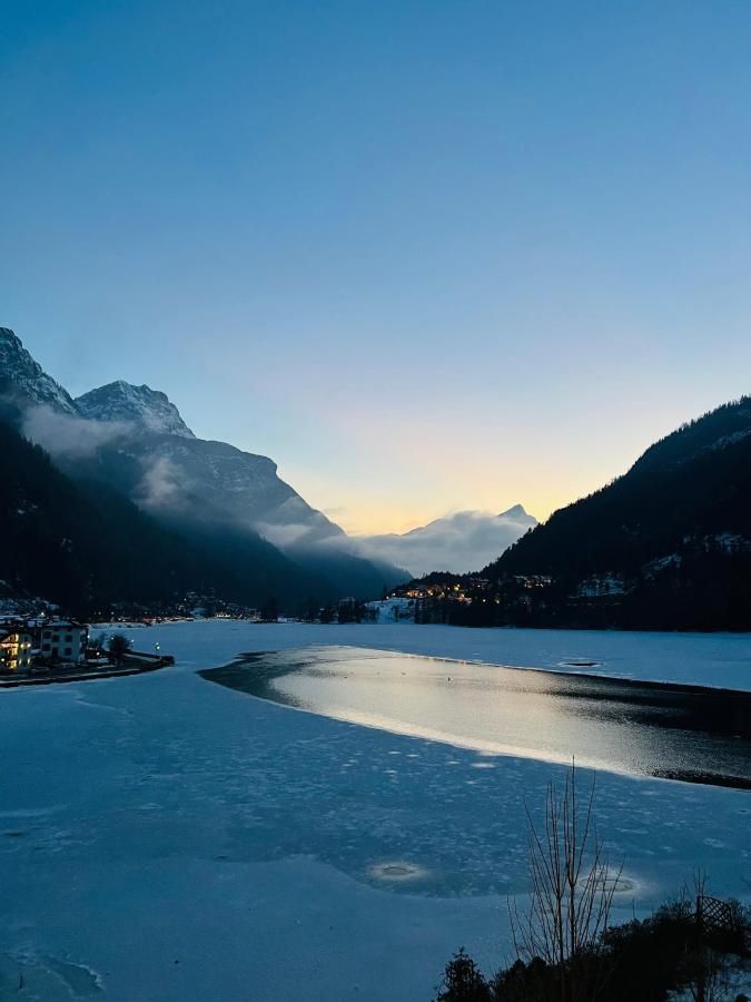 Lago ghiacciato con montagne, luci della città e cielo azzurro al tramonto.