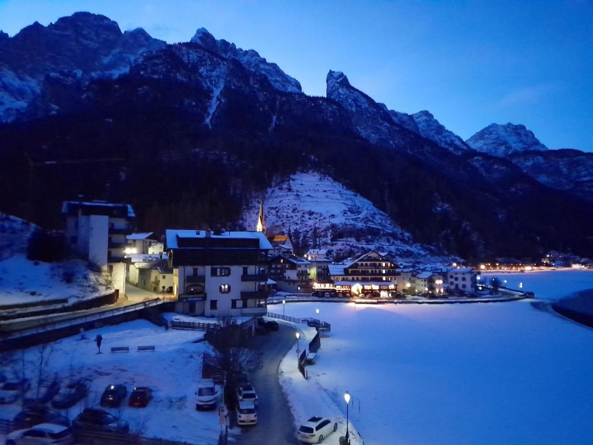 Città di montagna innevata al tramonto con luci, strada, lago ghiacciato e montagne alte e scure.