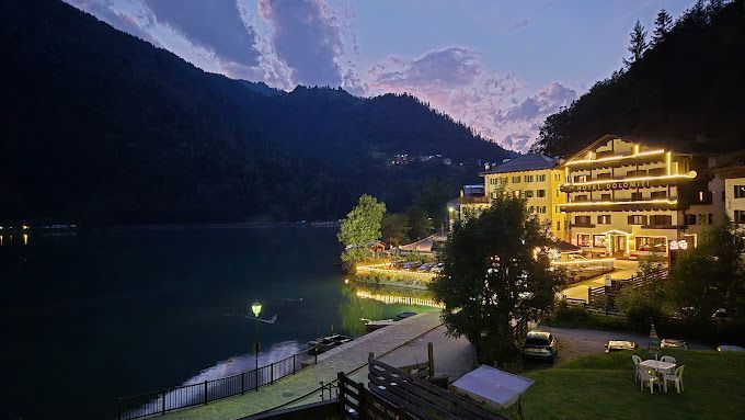Vista serale di una cittadina lacustre con edifici illuminati e montagne sullo sfondo.