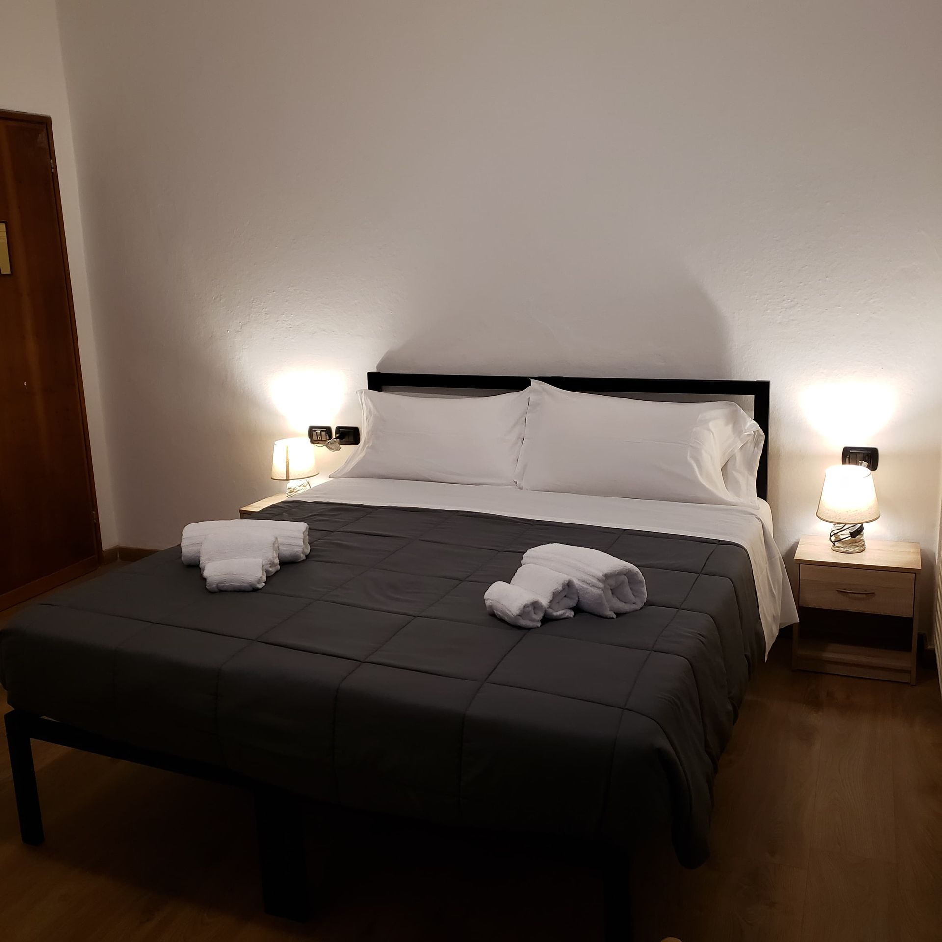 Camera da letto con letto, comodini e lampade. Lenzuola bianche, coperta grigio scuro e asciugamani piegati.
