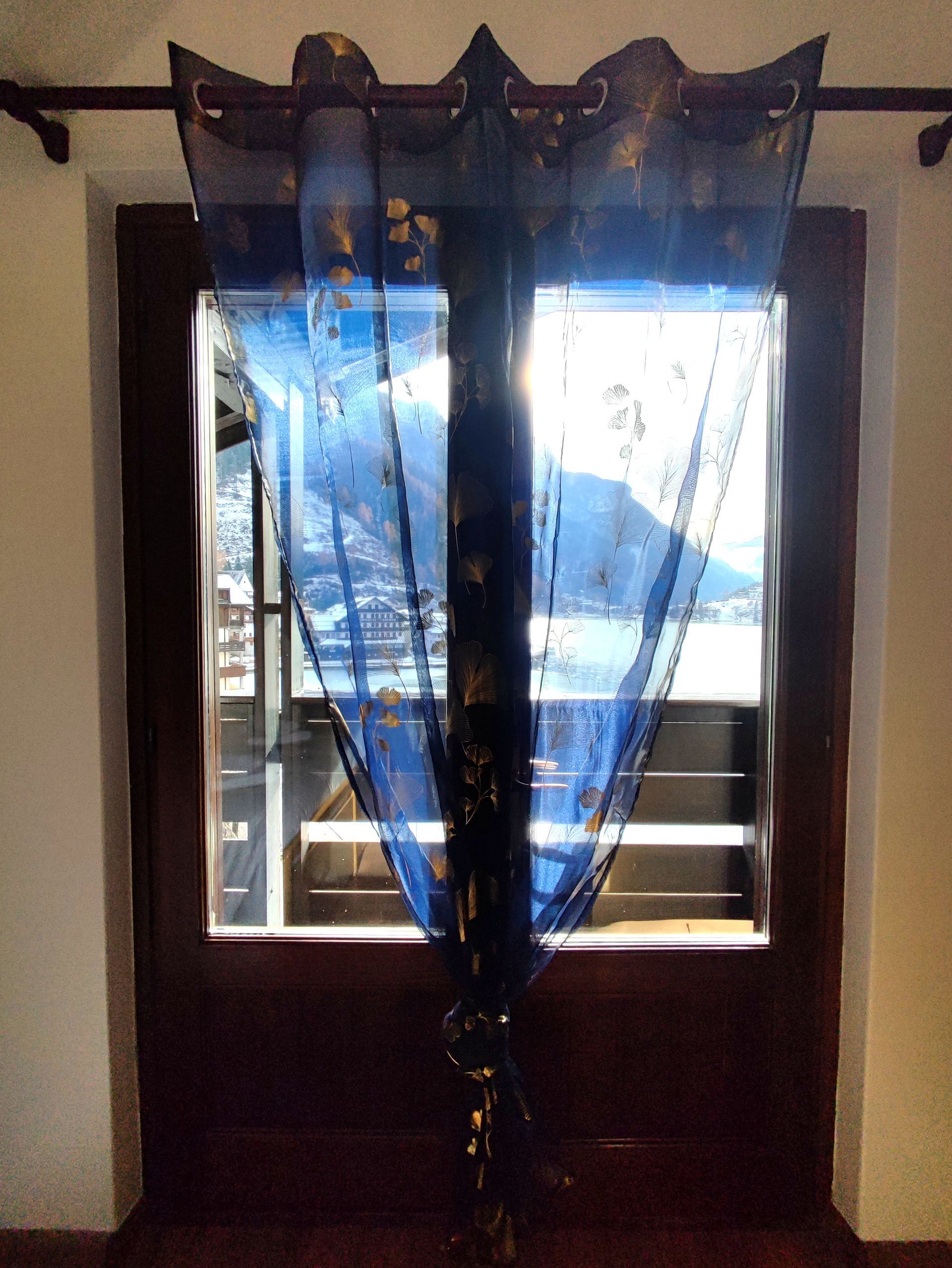 Tenda trasparente blu scuro con dettagli dorati sopra una finestra, vista interna.
