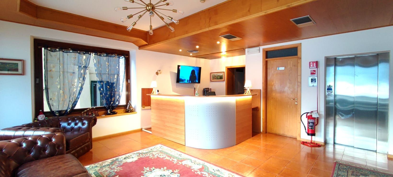 Hall dell'hotel con reception, area salotto e ascensore. Soffitto in legno, illuminazione calda.