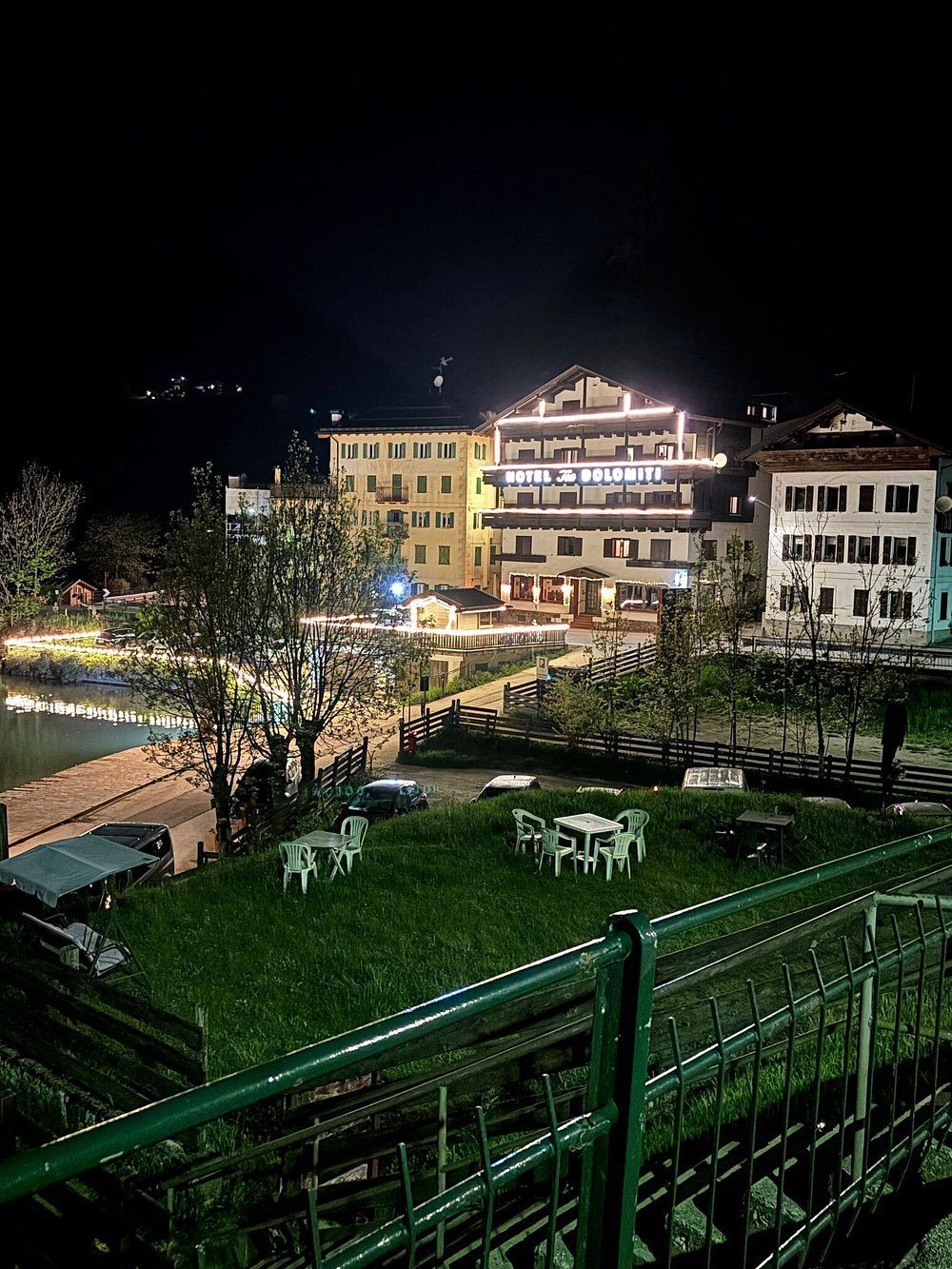 Vista notturna di edifici illuminati in una piccola città. Sono visibili anche alberi, prato verde con tavoli