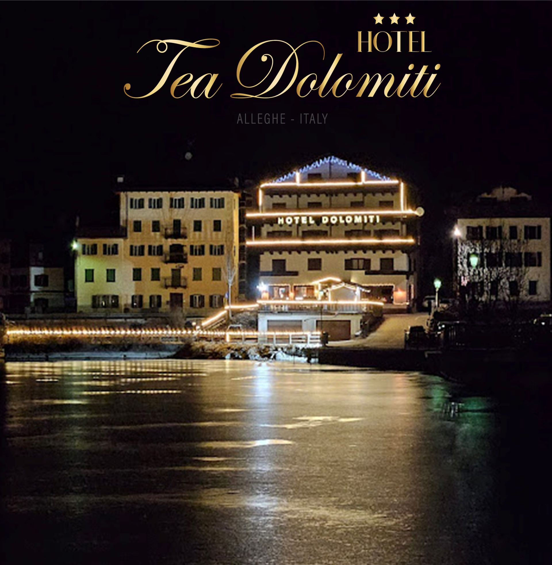 Hotel Tea Dolomiti, Alleghe, Italia, di notte. L'edificio illuminato si riflette nell'acqua.