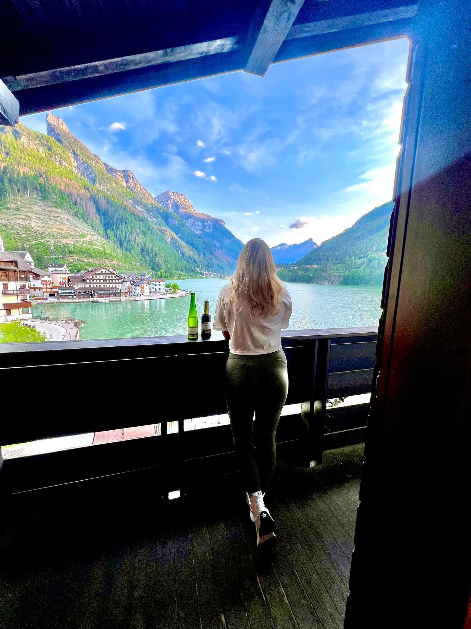 Donna che ammira il panorama panoramico del lago con le montagne da un balcone in legno.