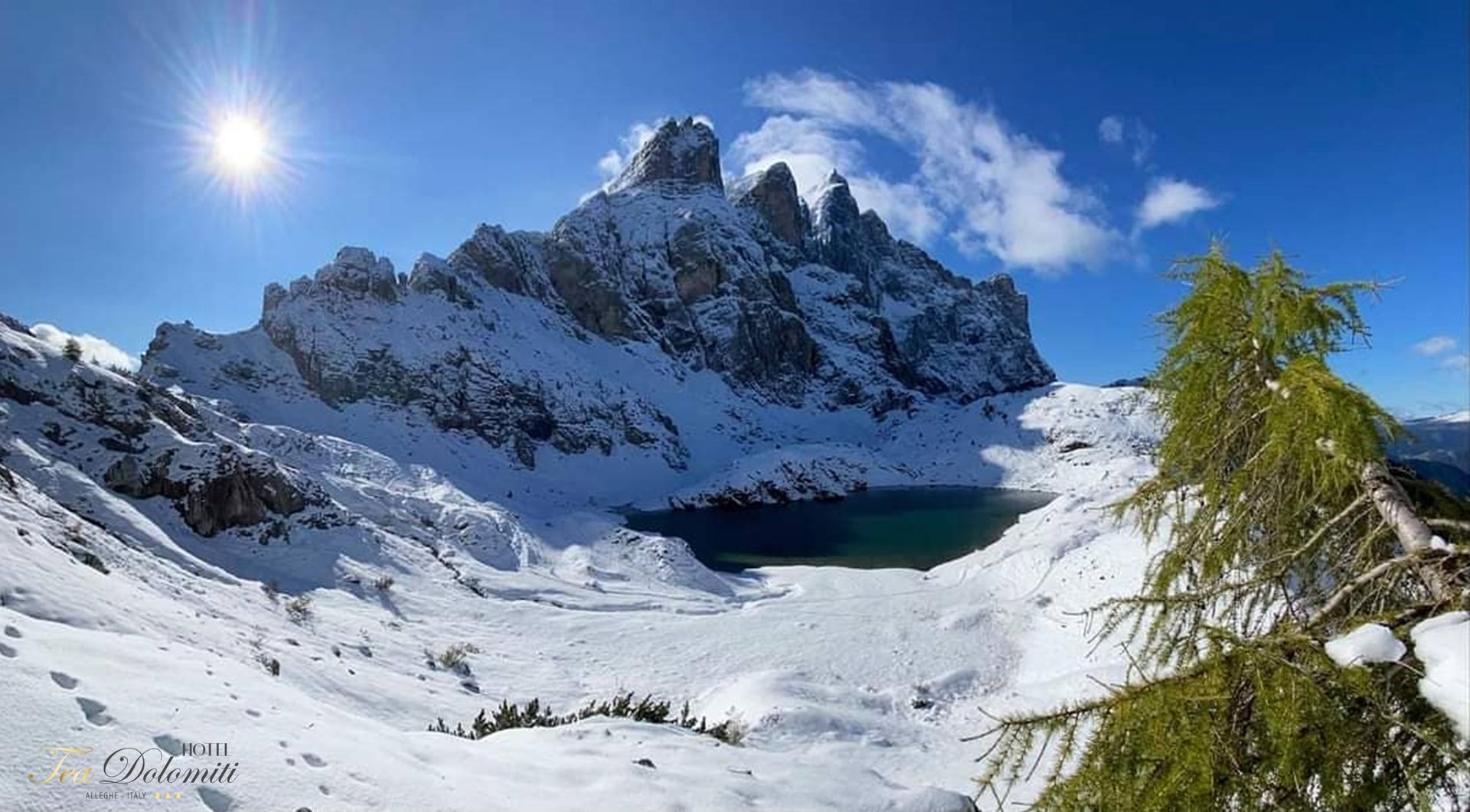 Catena montuosa innevata e lago ghiacciato sotto un sole splendente e un cielo azzurro.
