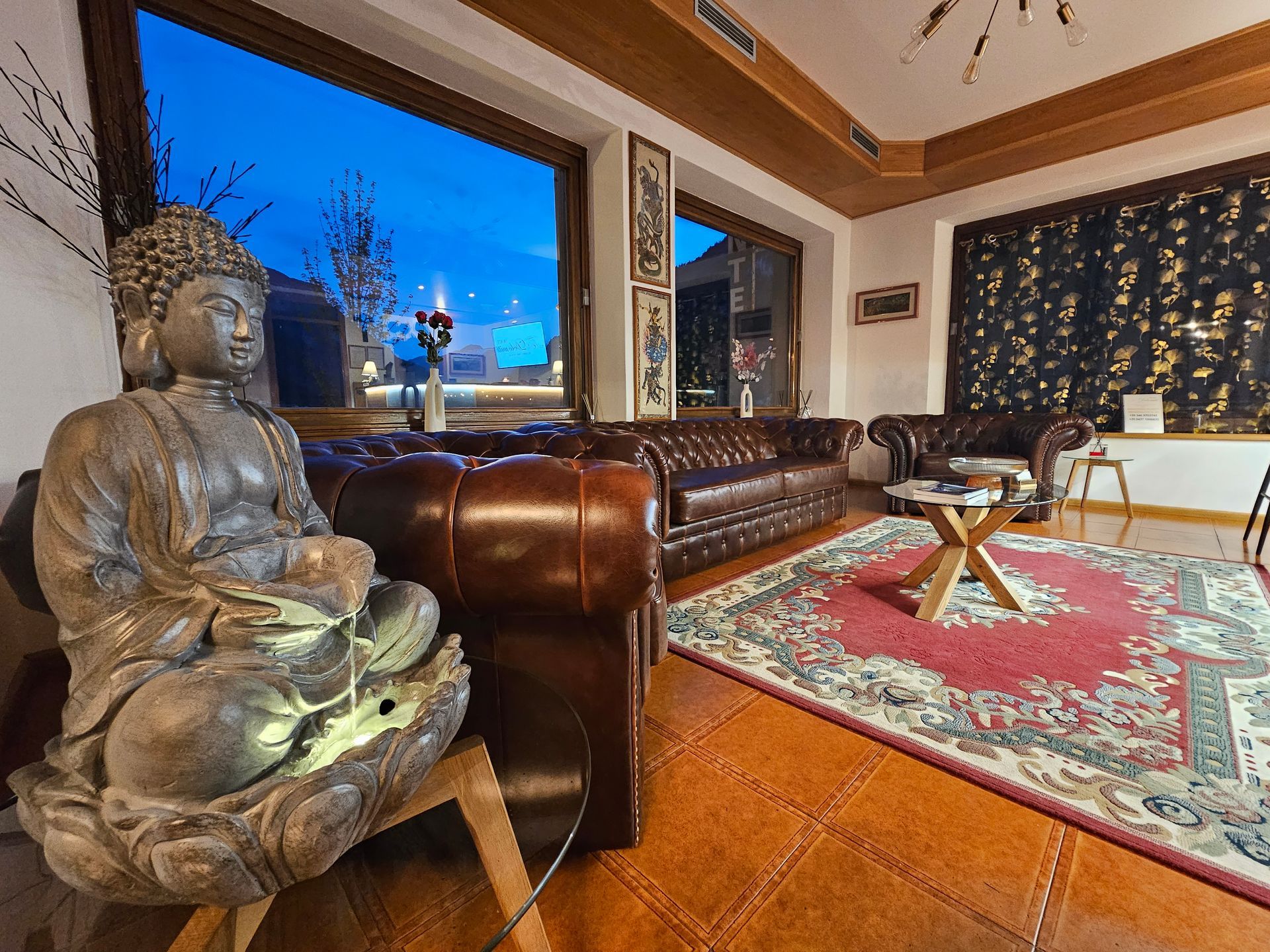 Statua del Buddha in un salotto con divani in pelle, un tappeto a fantasia e una grande finestra con vista sull'esterno.