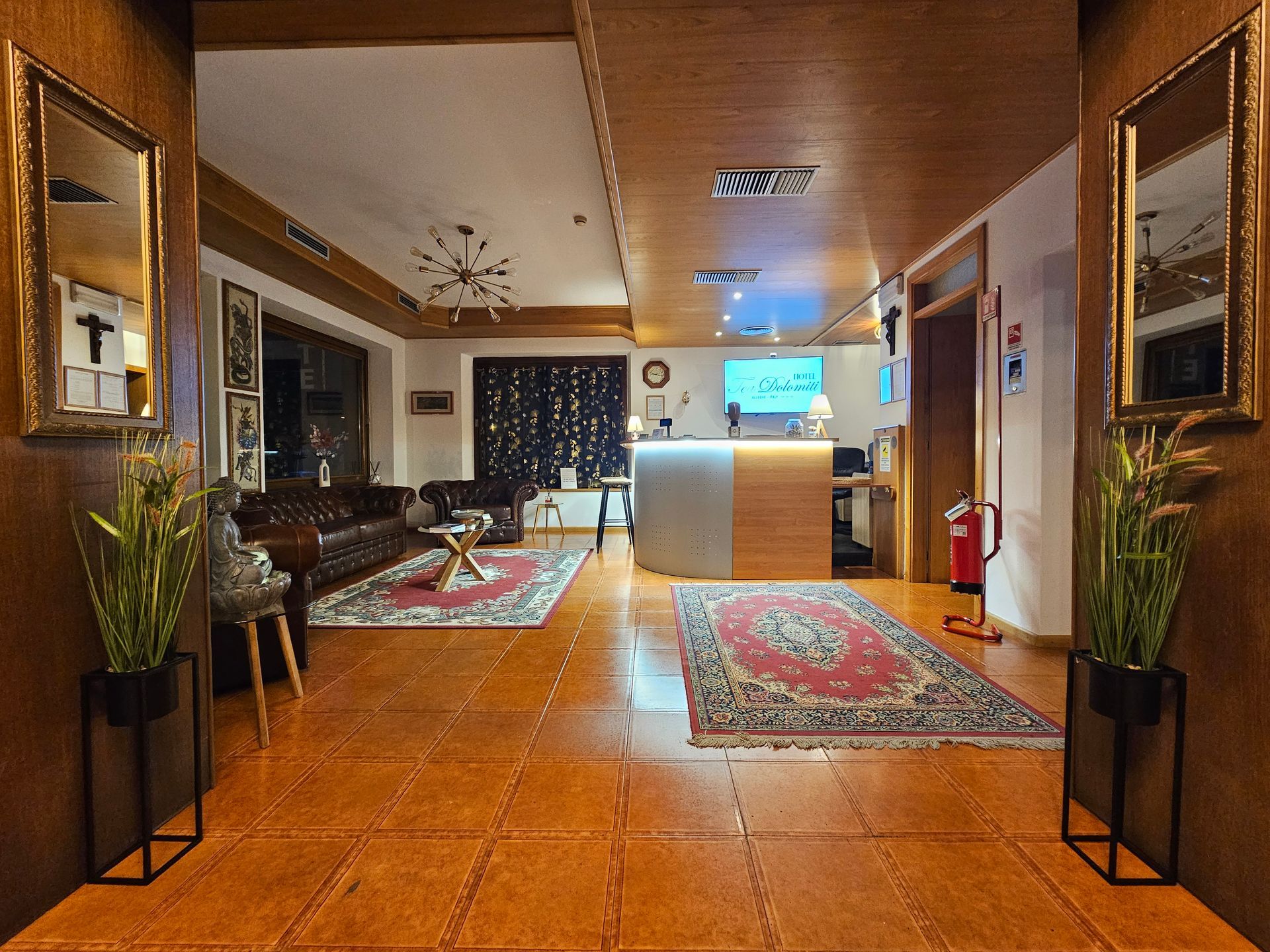 Hall dell'hotel con reception, area salotto e piante decorative. Tonalità marrone e oro.