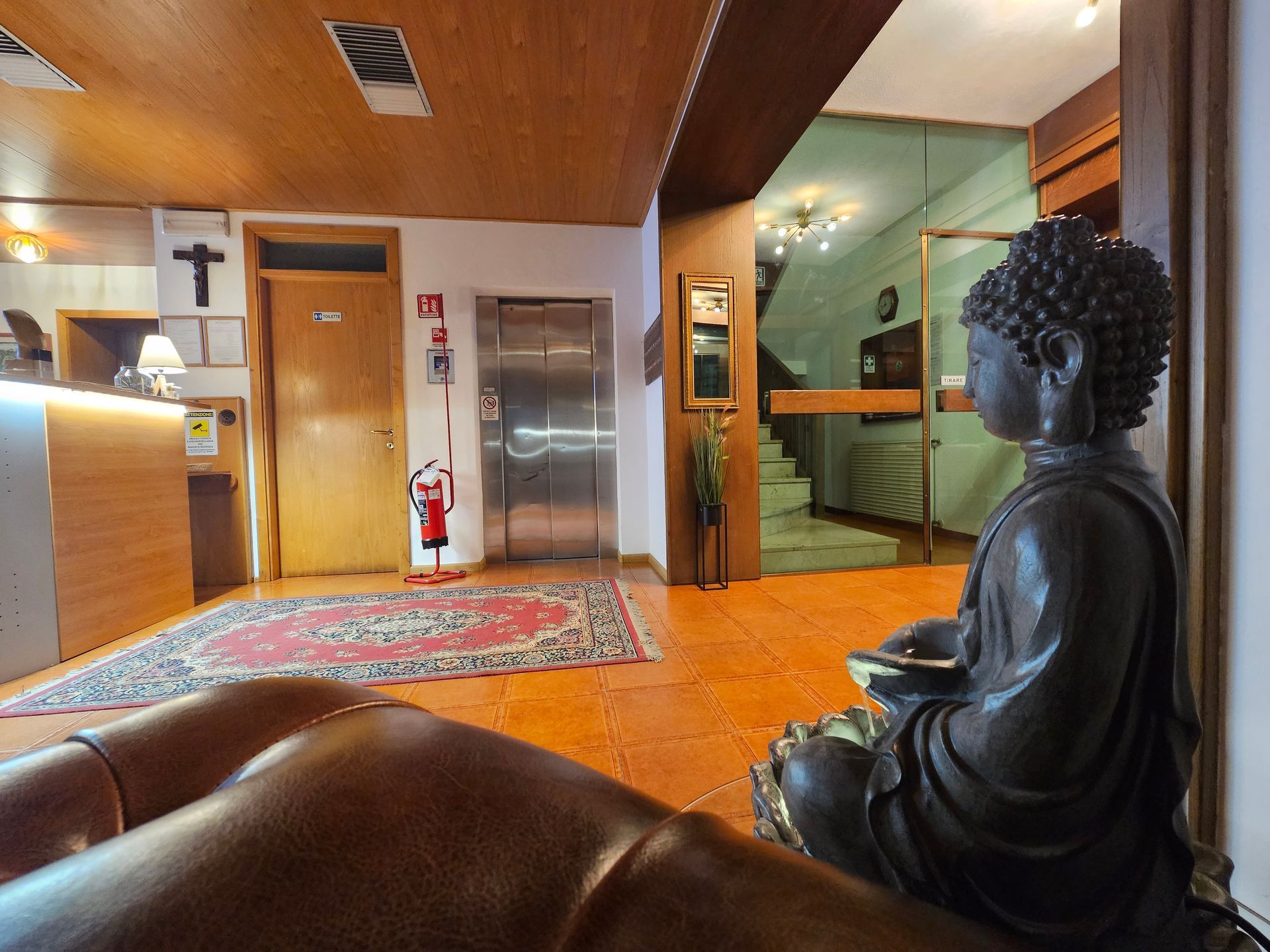 Hall dell'hotel con statua del Buddha, ascensore, reception e scale per un'altra stanza.