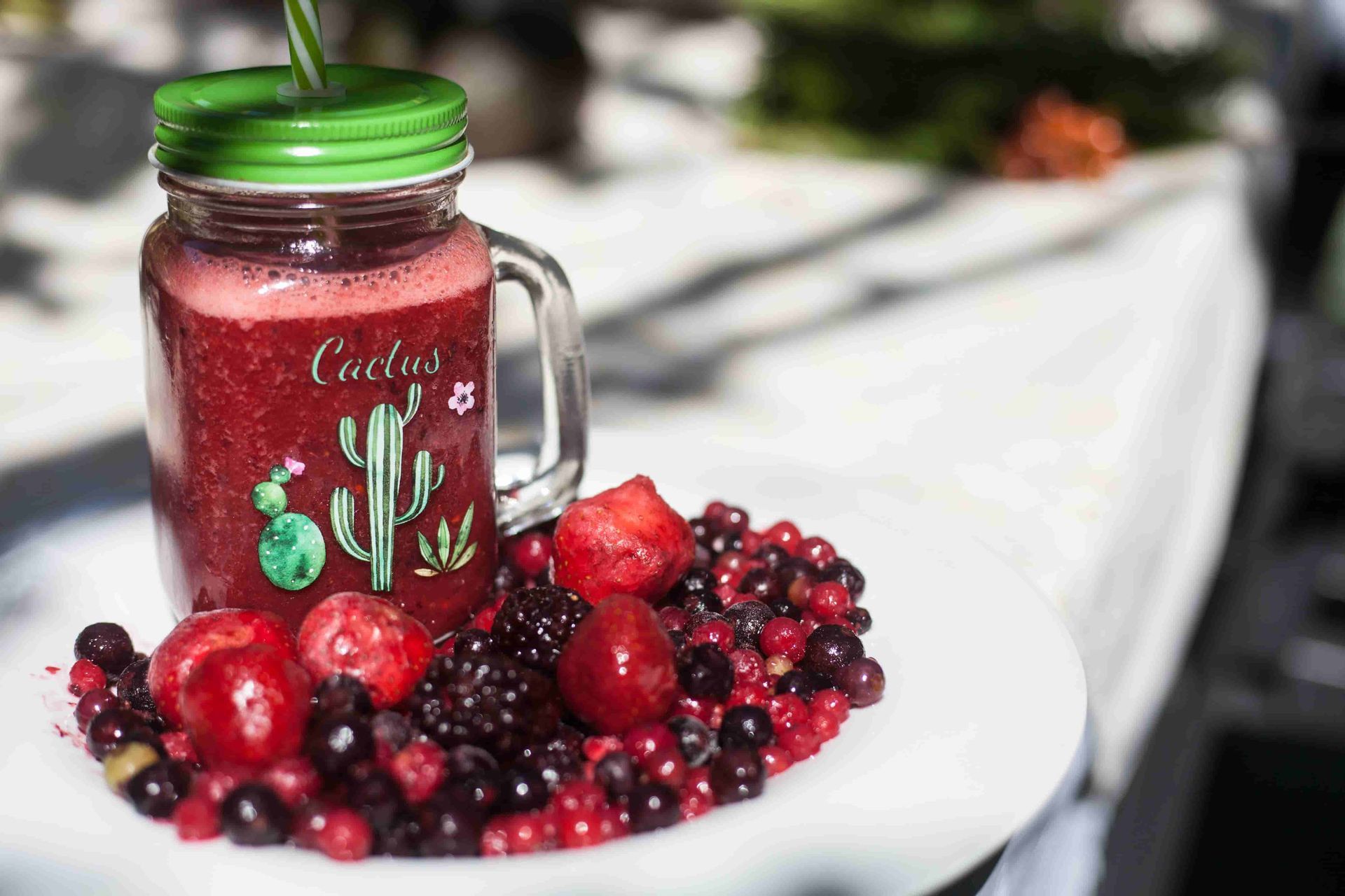 Un batido de bayas en un frasco de vidrio con una pajita, rodeado de bayas frescas en un plato blanco.