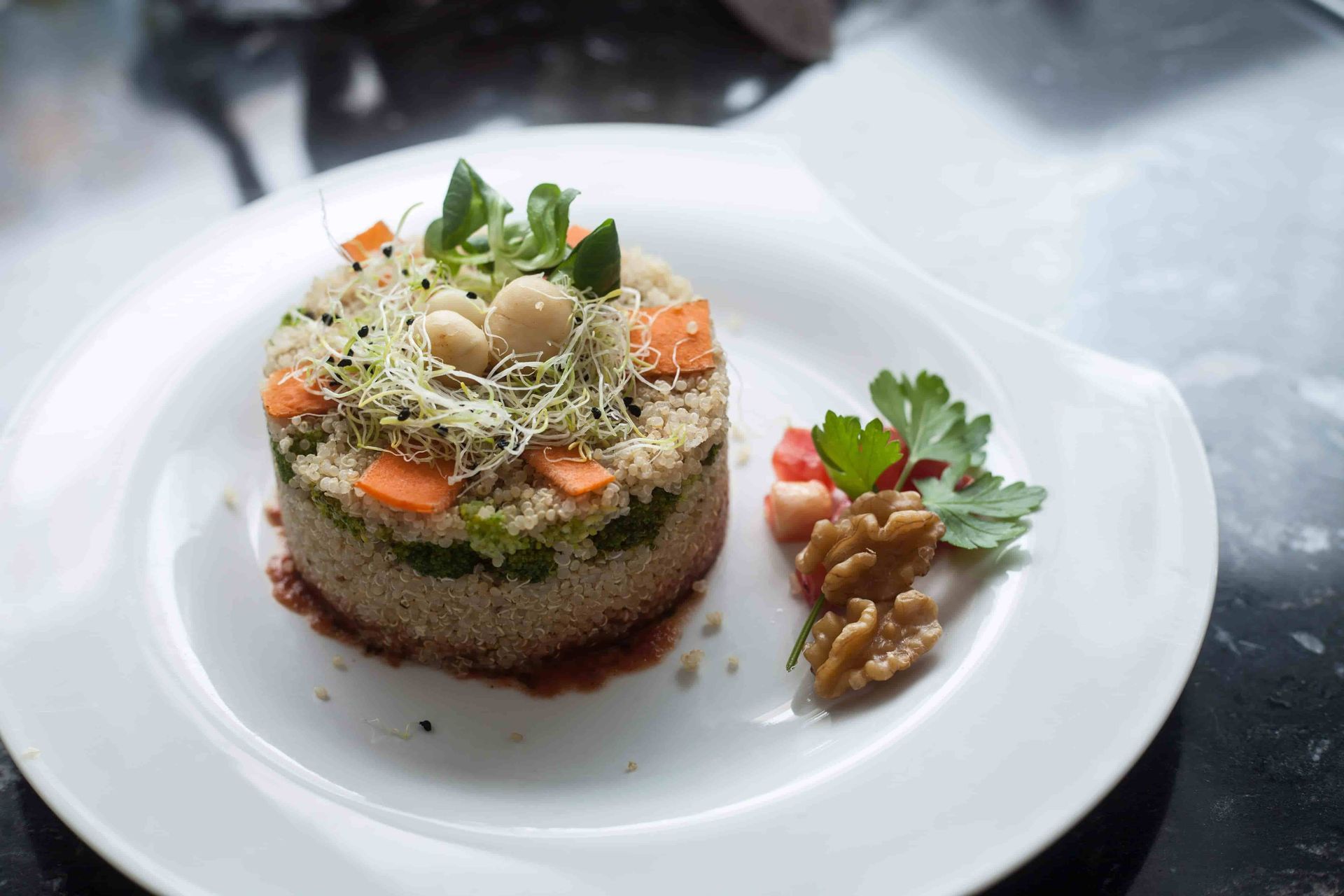 Ensalada cilíndrica de cuscús con zanahorias, brotes, nueces y verduras en un plato blanco.