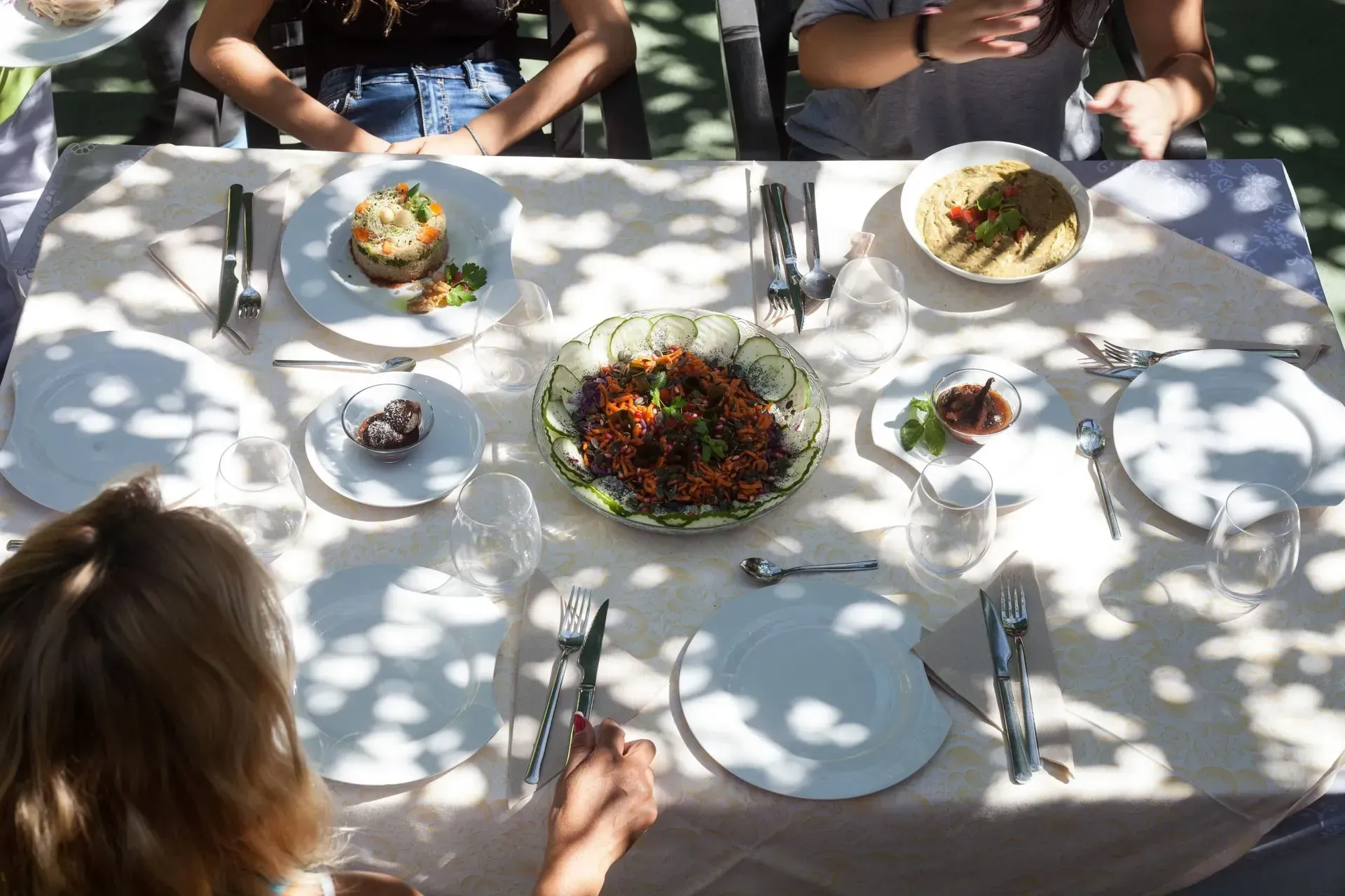 Mesa puesta con comida y cuatro personas sentadas, disfrutando de una comida al aire libre.
