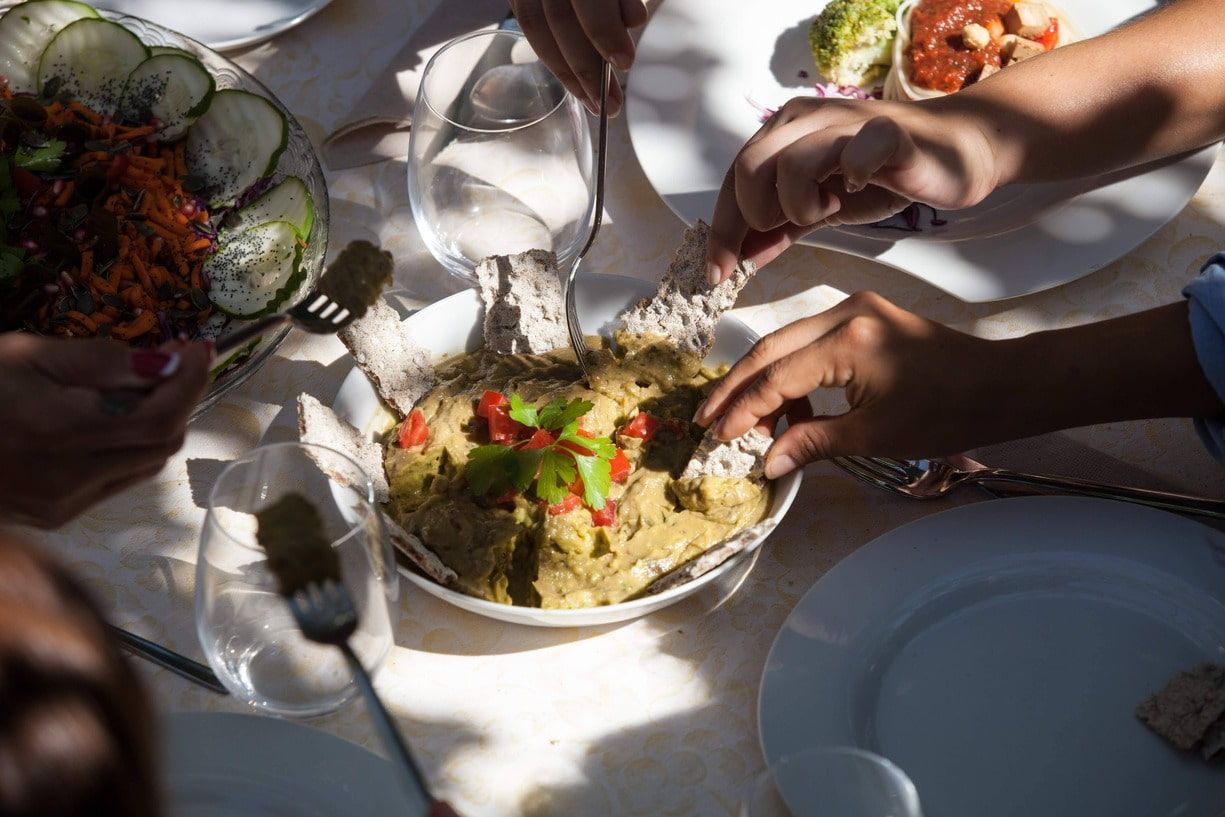 Personas buscando comida en una mesa, incluyendo salsa con pan y ensaladas.