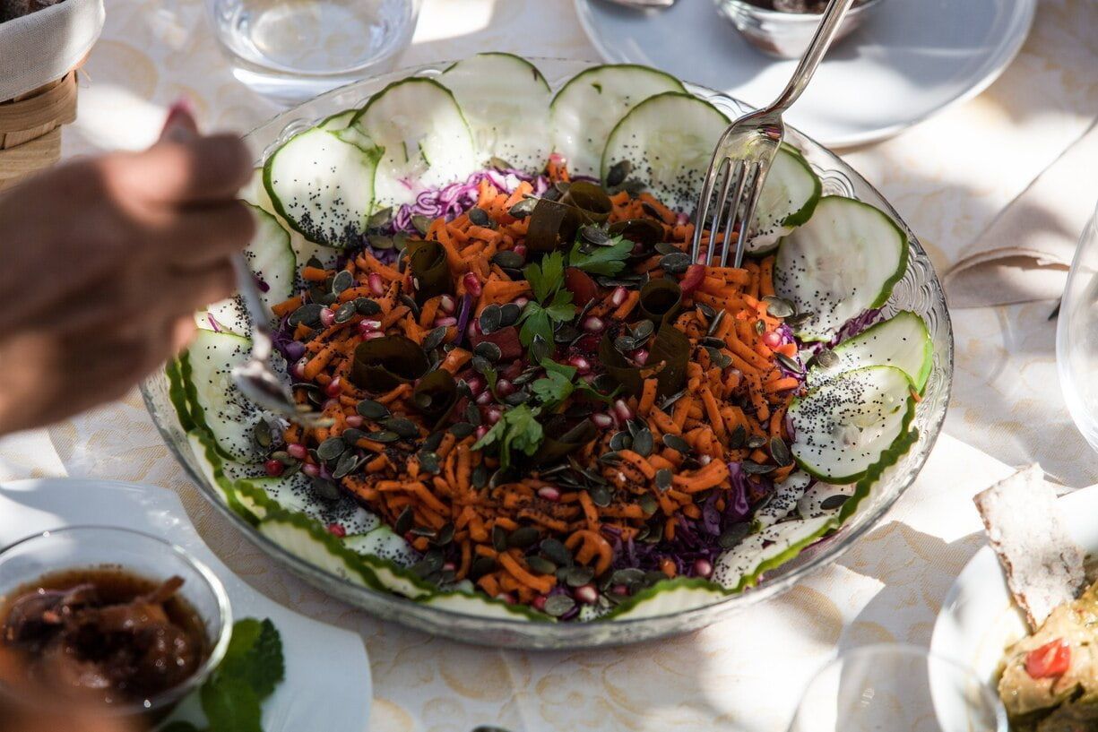 Ensaladera grande con pepinos, zanahorias ralladas, verduras y una mano con un tenedor.