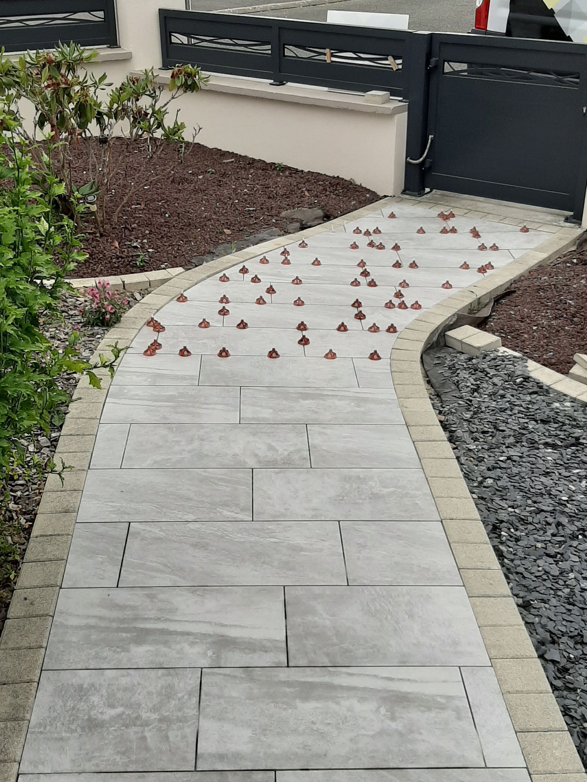 Allée en pierre grise parsemée de baies rouges, bordée de pavés et de gravier, menant à une clôture.