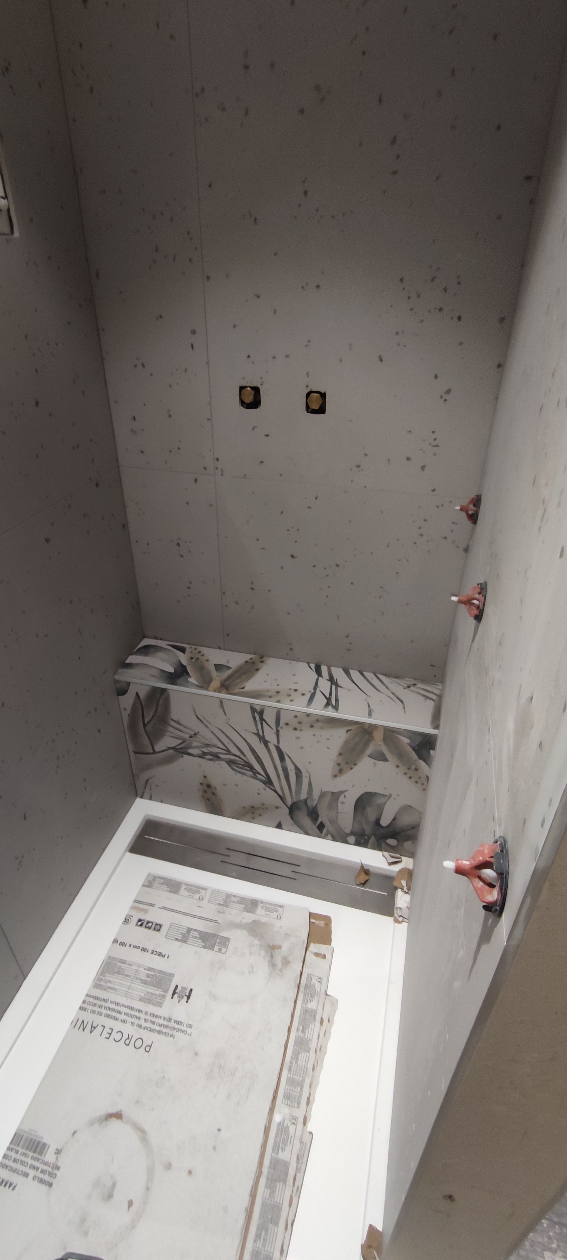 Salle de bains inachevée avec murs en béton apparent. Deux prises électriques sont visibles.