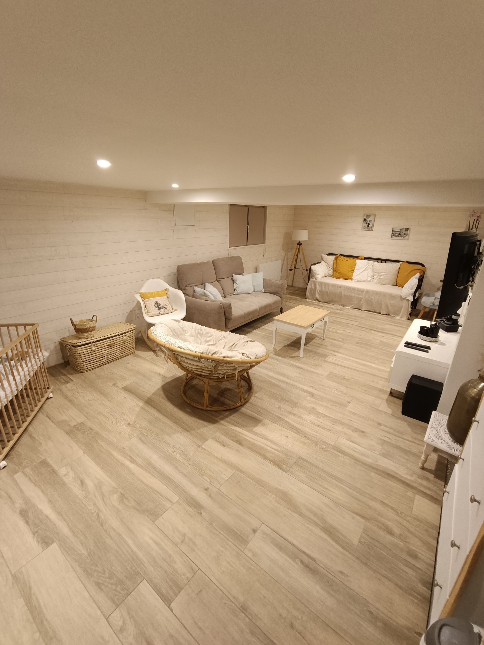 Salon avec parquet clair, plusieurs canapés, un fauteuil en osier et une table basse blanche.