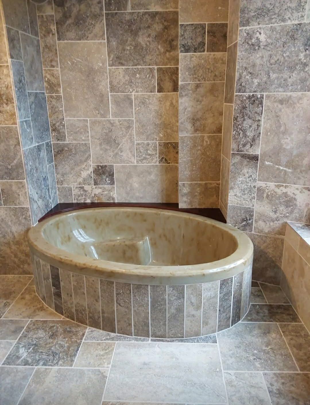 Baignoire ovale encastrée dans une alcôve carrelée en pierre. La baignoire est entourée et adossée à des murs et un sol en pierre assortis.