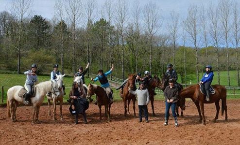 Groupe de cavaliers posant dans une arène en terre battue avec des arbres en arrière-plan