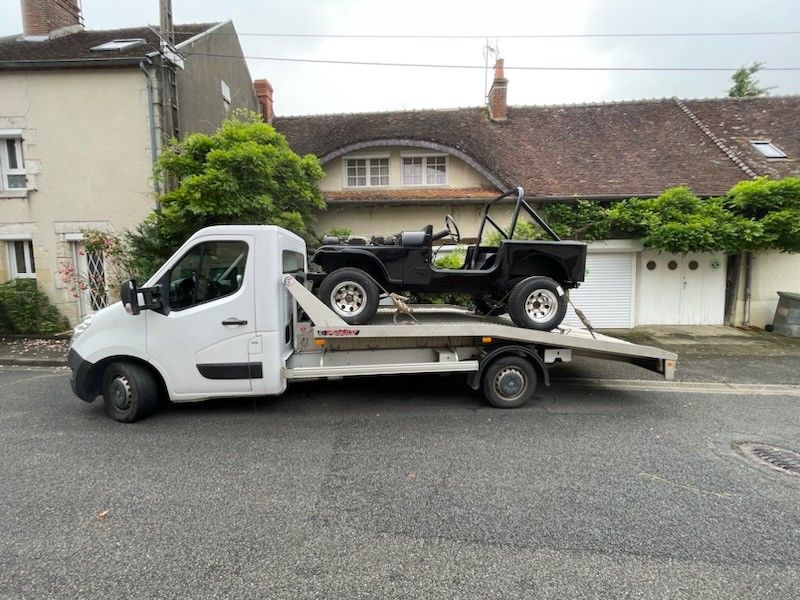 Une Jeep noire sur une dépanneuse, garée dans la rue devant une maison.