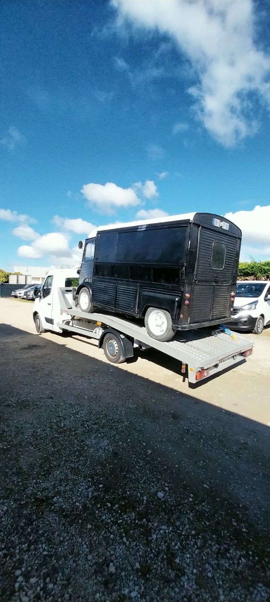 Un camion noir sur une dépanneuse à plateau par une journée ensoleillée. Ciel bleu, nuages ​​blancs et asphalte sombre.
