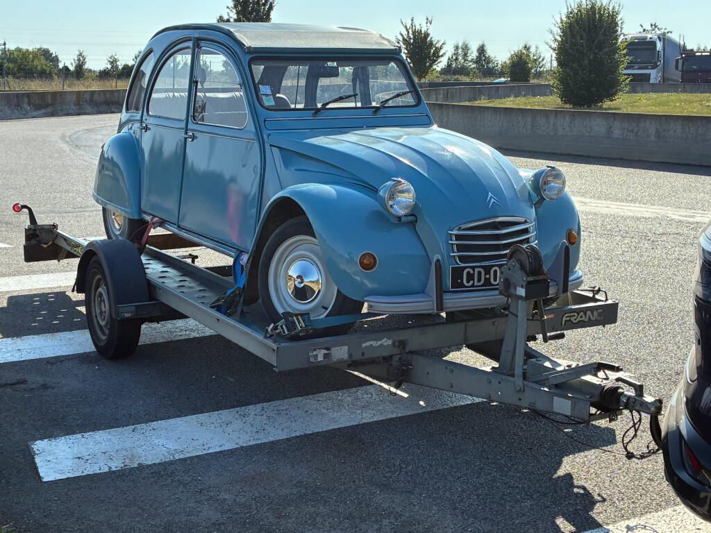 Une Citroën 2 CV bleue vintage sur une remorque dans un parking.