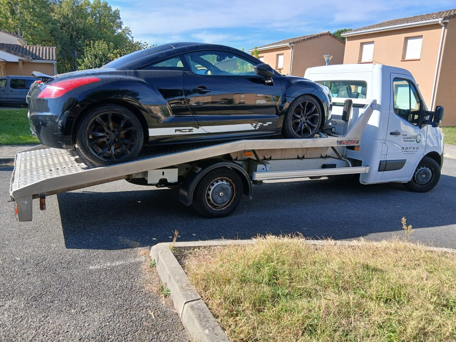 Une voiture de sport noire chargée sur une dépanneuse blanche sur un parking goudronné.