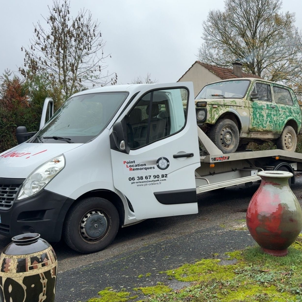 Une dépanneuse blanche transporte un SUV vert rouillé en bord de route.