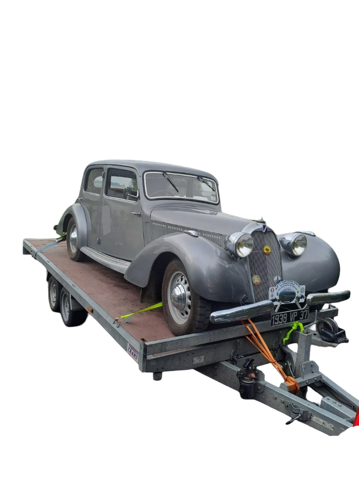 Voiture ancienne grise fixée sur une remorque plateau, prête pour le transport.