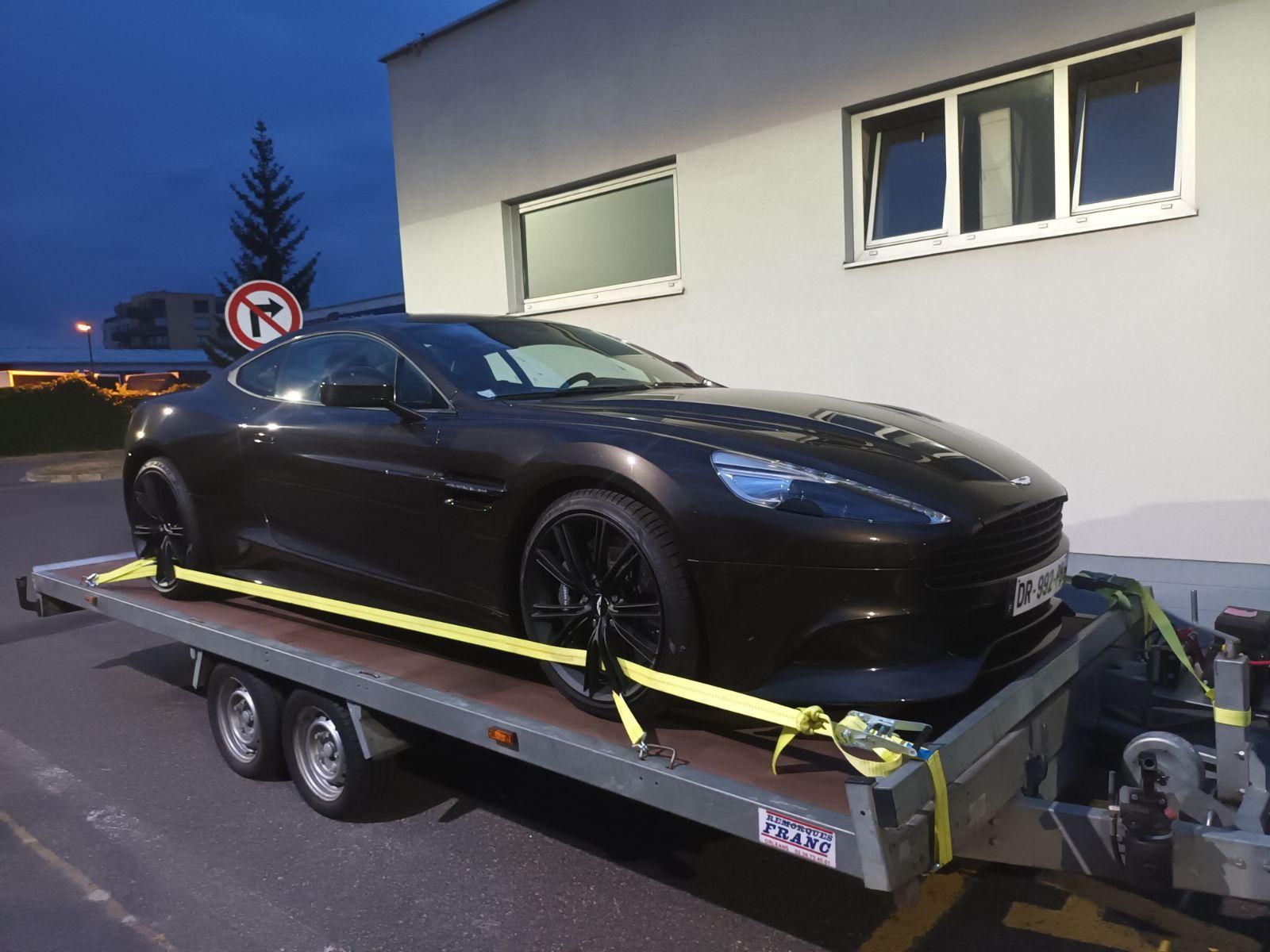 Une voiture de sport est immobilisée sur une remorque, à l'extérieur d'un bâtiment au crépuscule.