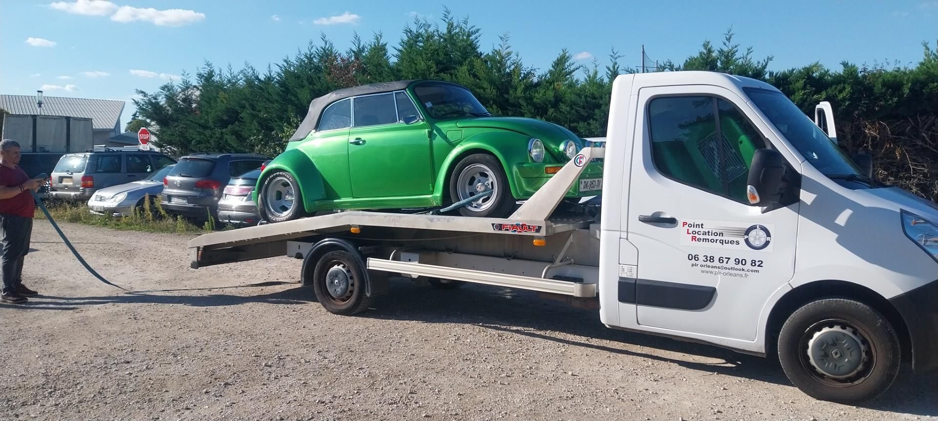 Une décapotable verte sur une dépanneuse. Voitures garées et arbres en arrière-plan.