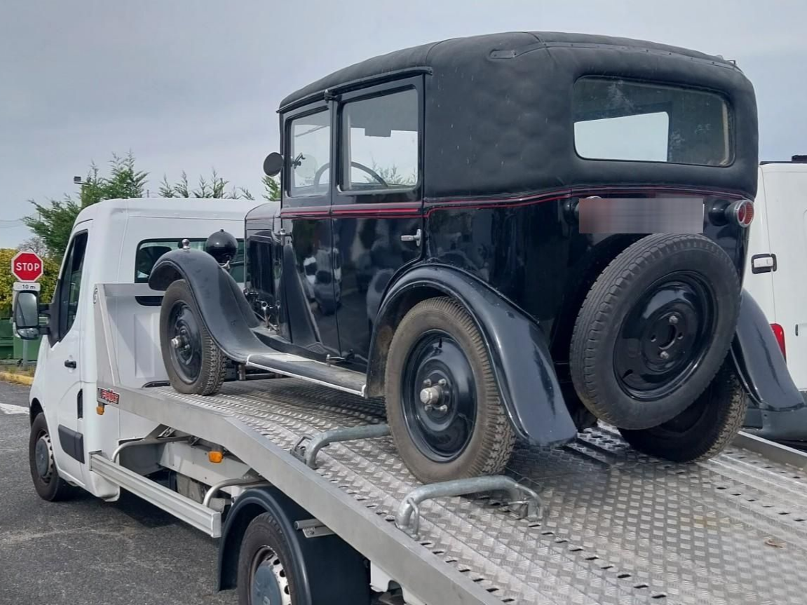Voiture ancienne noire sur le plateau d'une dépanneuse blanche ; ciel couvert.